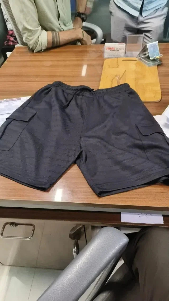 Black casual cargo shorts for men laid flat on a wooden table showing side pockets