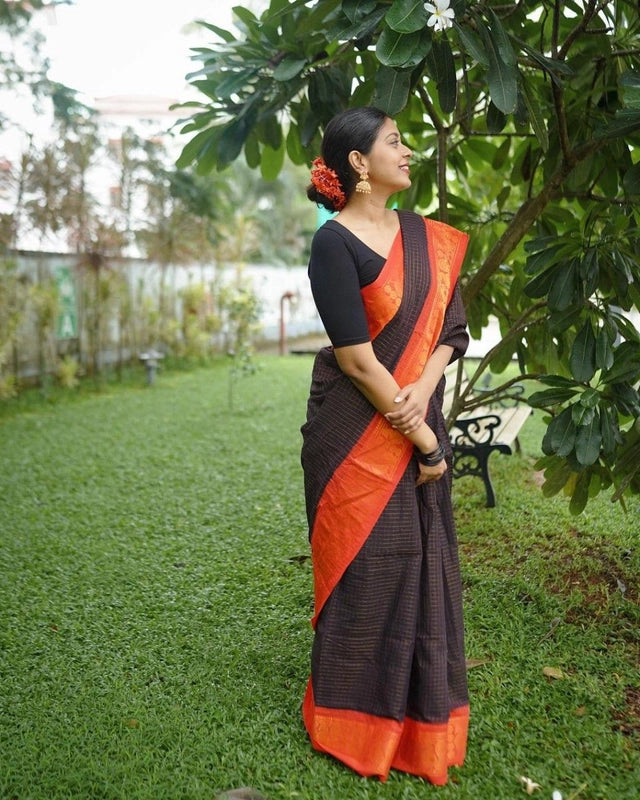 Woman in a garden wearing a black saree with bright orange border and floral bun, Banarasi silk saree for women