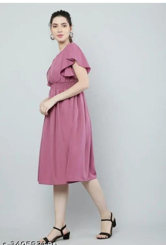 Model in a knee length pink fit and flare dress for women with flutter sleeves smocked waist and black sandals