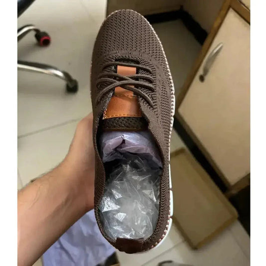 Hand holding brown mesh casual shoes with lace-up design and cushioned sole